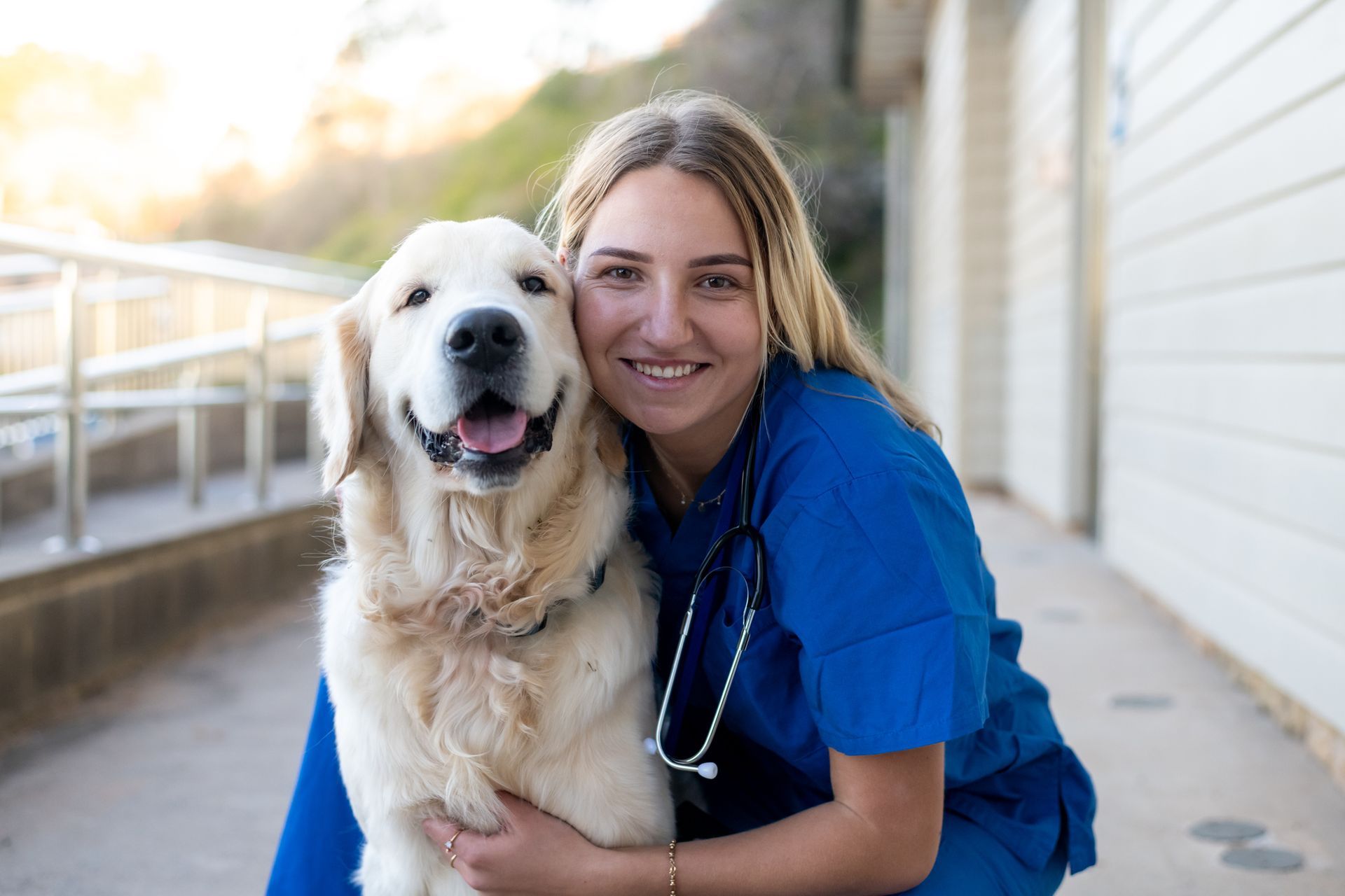 Veterinarian poses with a golden retriever outside a clinic. 