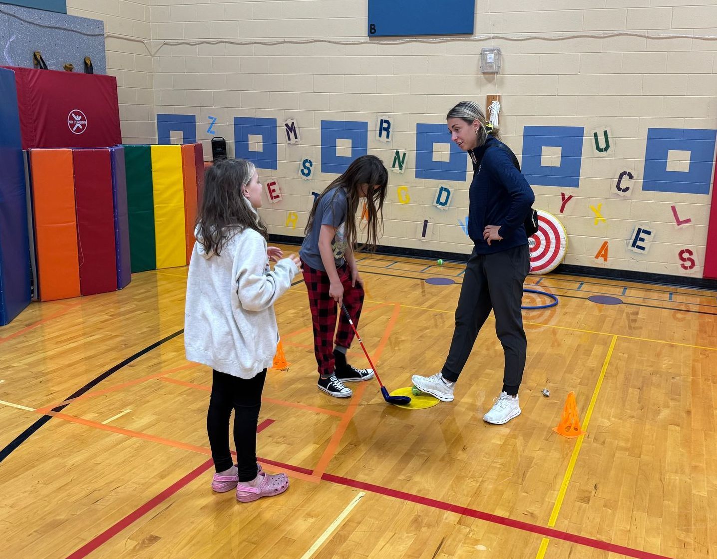 A group of young girls are playing a game of hockey in a gym.