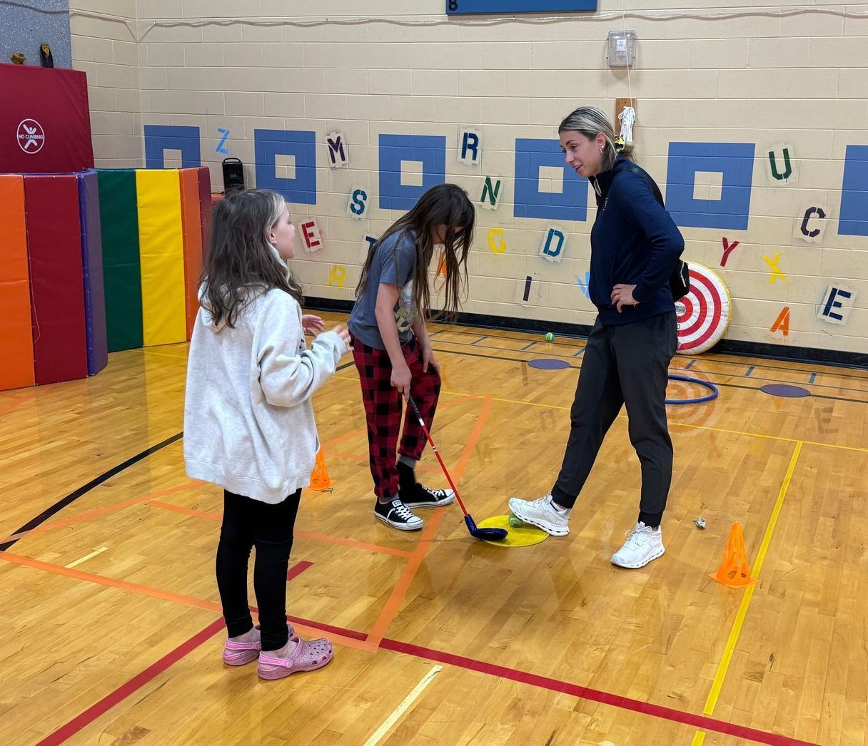 A group of young girls are playing a game of hockey in a gym.