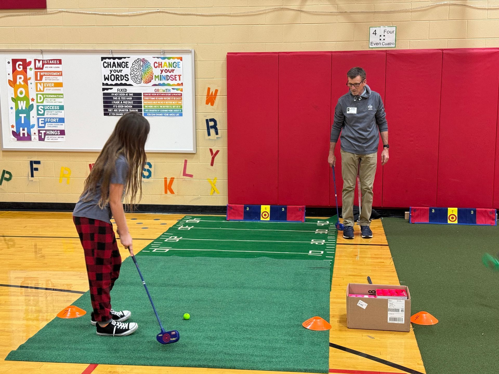 A man and a girl are playing golf in a gym.