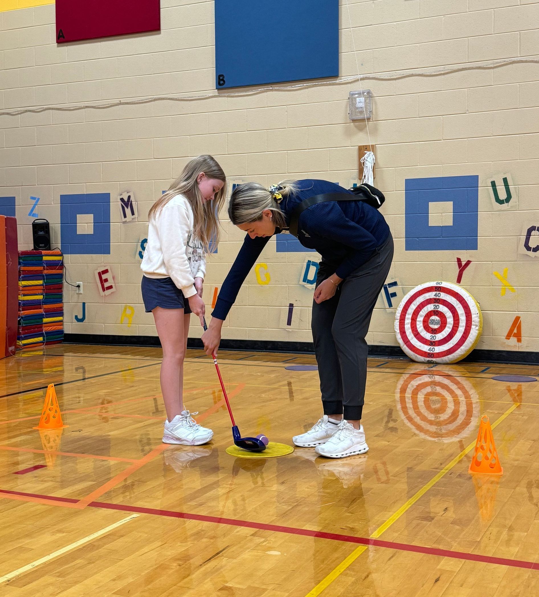 A woman and a girl are playing a game of golf in a gym.