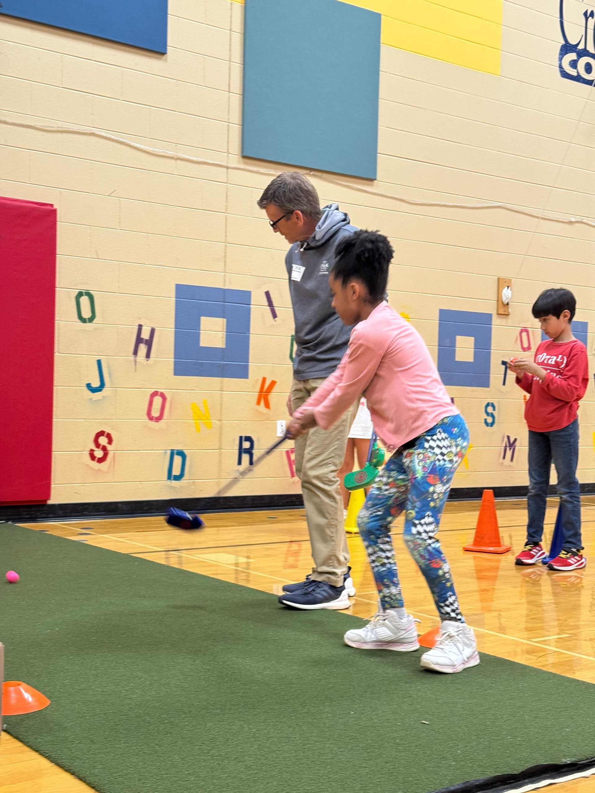 A man and a girl are playing a game of golf in a gym.