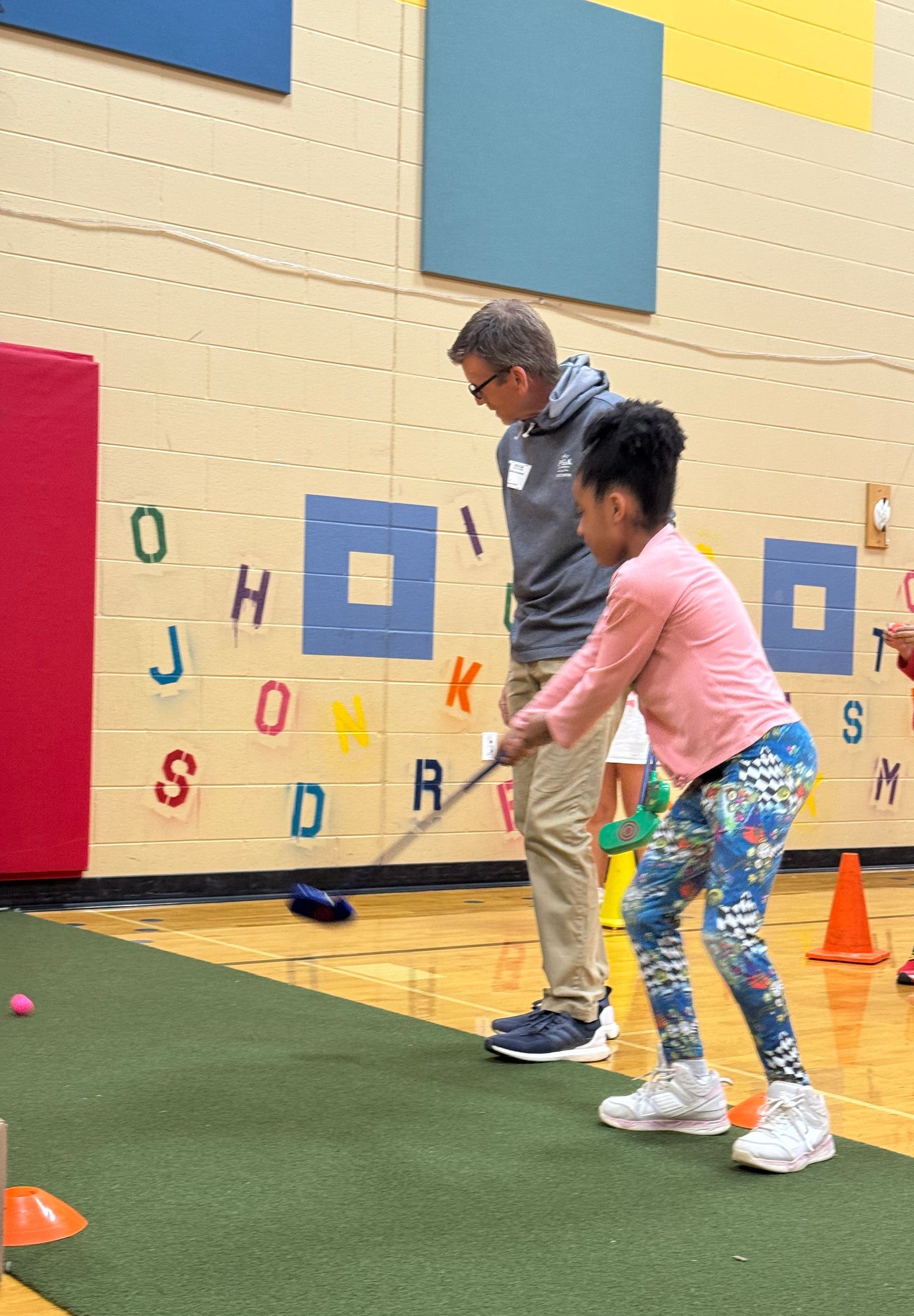 A man and a girl are playing a game of golf in a gym.