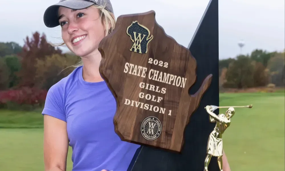 A woman is holding a plaque that says state champion girls golf division 1