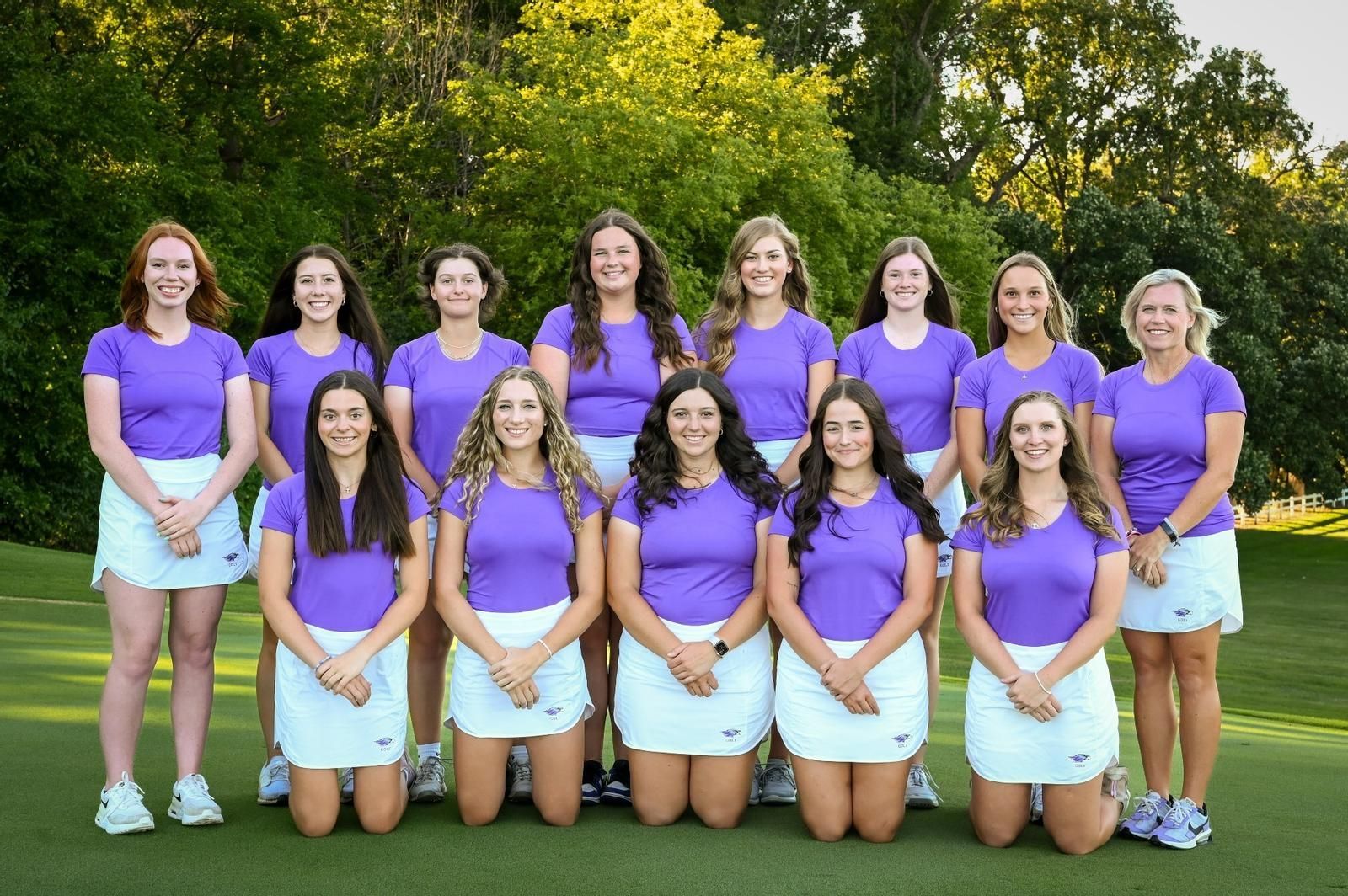 A group of women in purple shirts and white skirts are posing for a picture on a golf course.