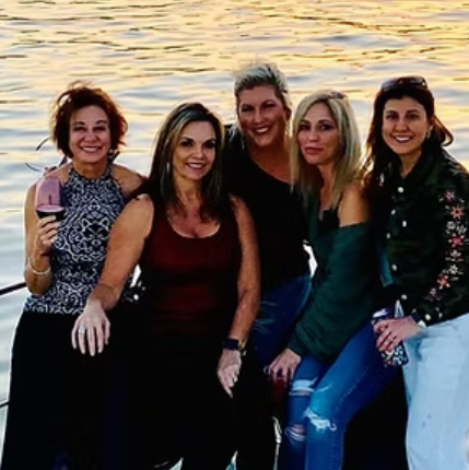 A group of women are posing for a picture in front of a body of water.