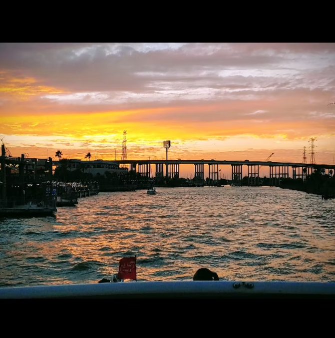 A sunset over a body of water with a bridge in the background.