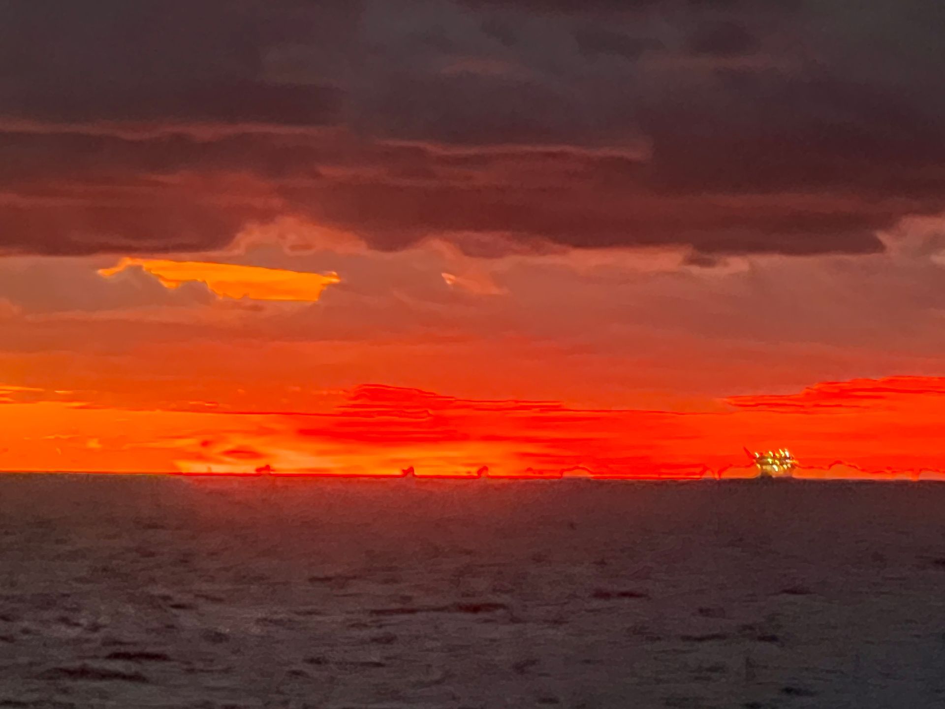 A sunset over the ocean with a boat in the distance.