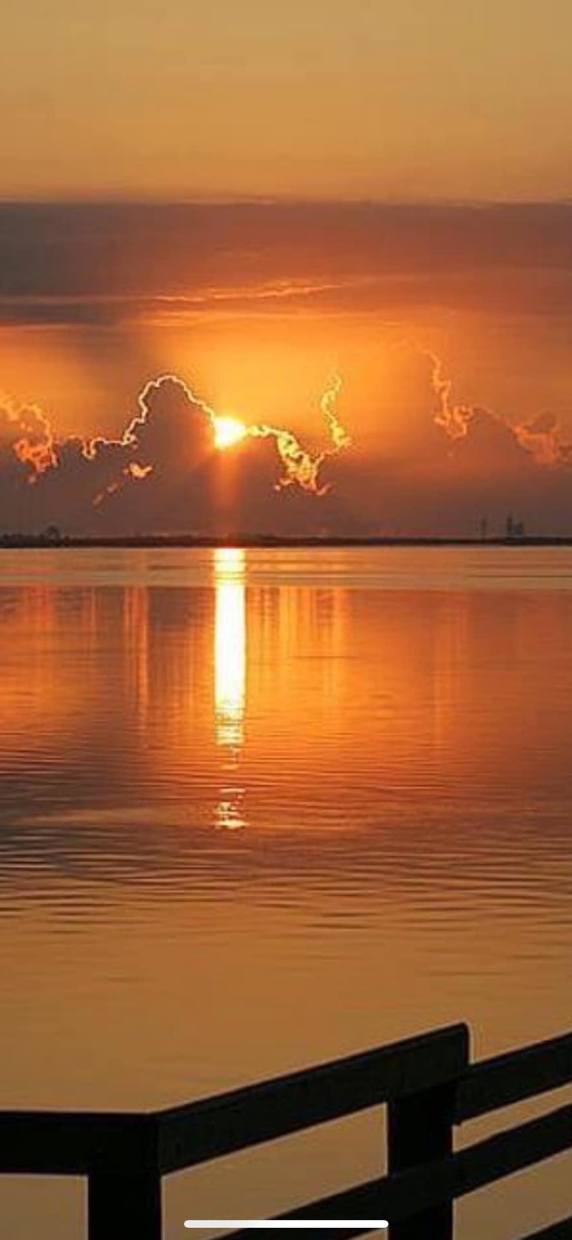 A sunset over a body of water with a fence in the foreground.