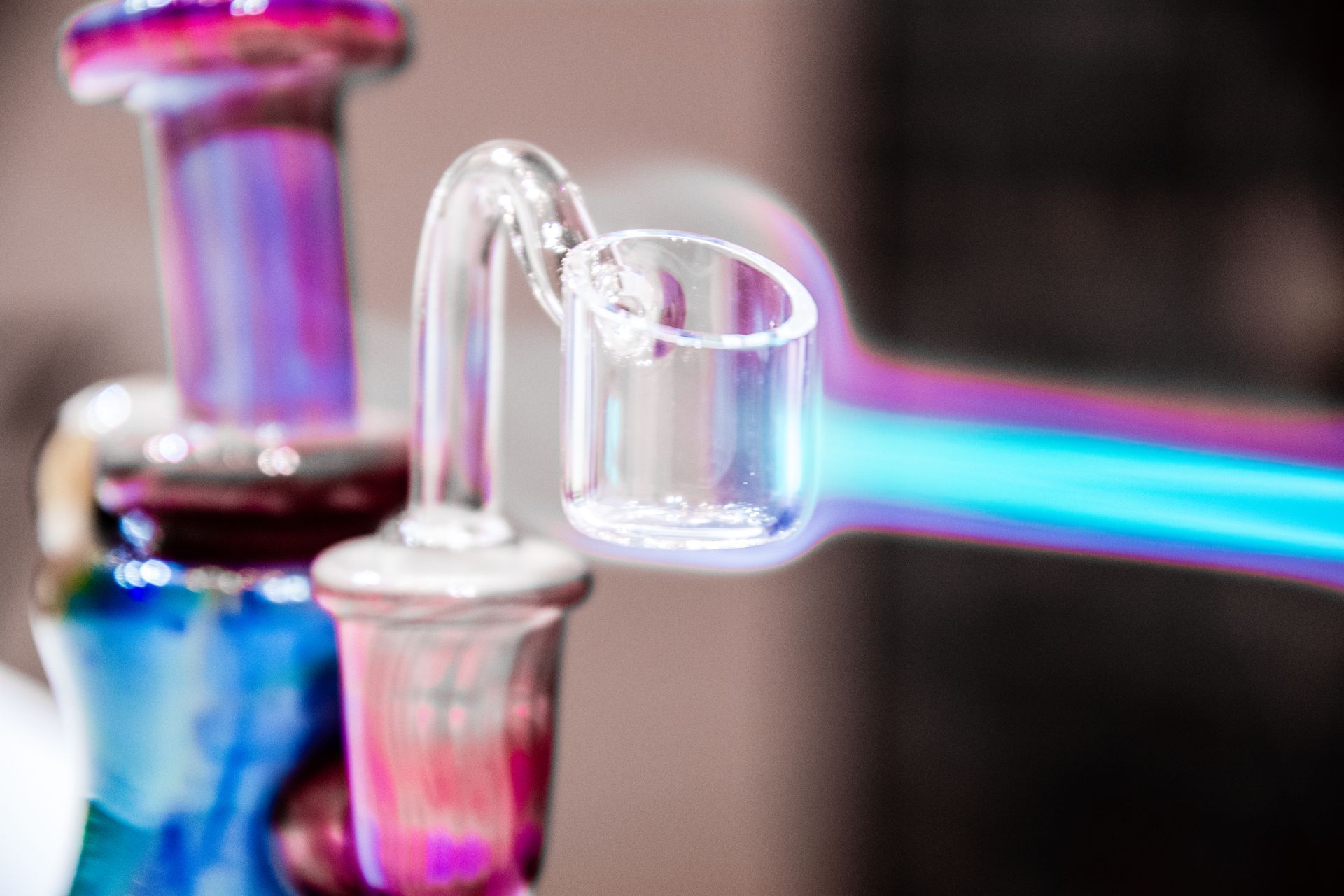 A glass banger being heated by a blue flame, attached to the joint of a colorful glass water pipe.