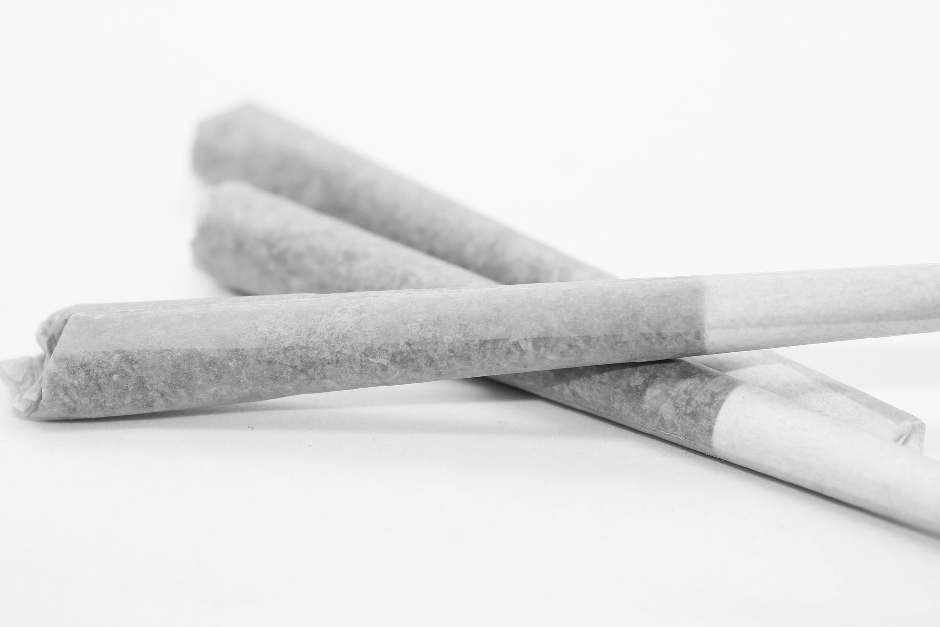 Three hand-rolled cigarettes with white filter tips arranged in a pile against a white background.