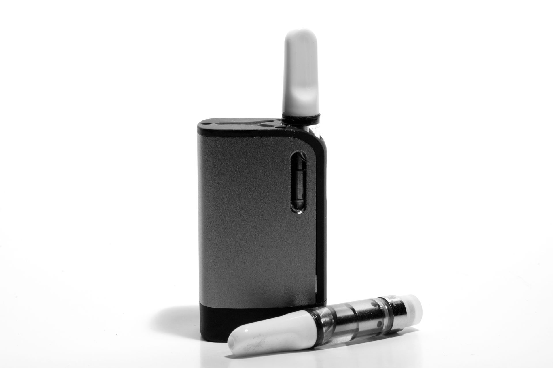 A gray vape battery device with an attached cartridge, and a spare clear cartridge lying in front on a white background.