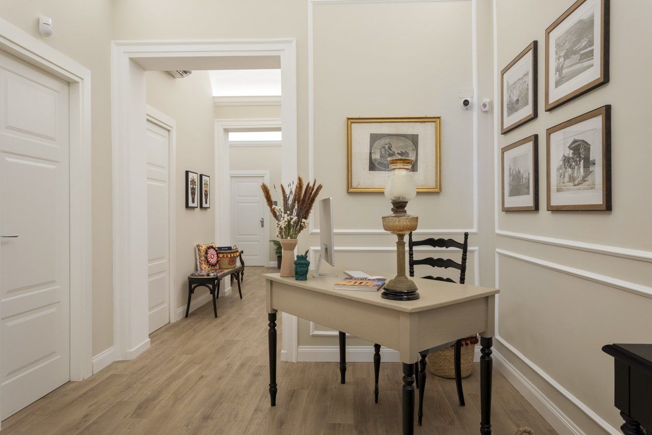 Corridoio con scrivania, opere d'arte e finiture bianche. Pavimento in legno chiaro, porte bianche, pareti neutre.