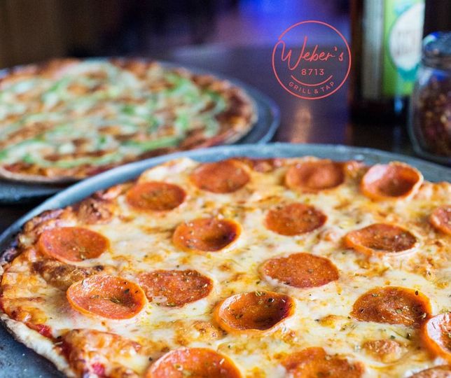 A pepperoni pizza is on a pan next to a green pepperoni pizza.