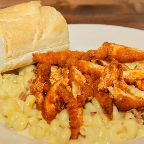 A plate of macaroni and cheese with chicken and a loaf of bread.