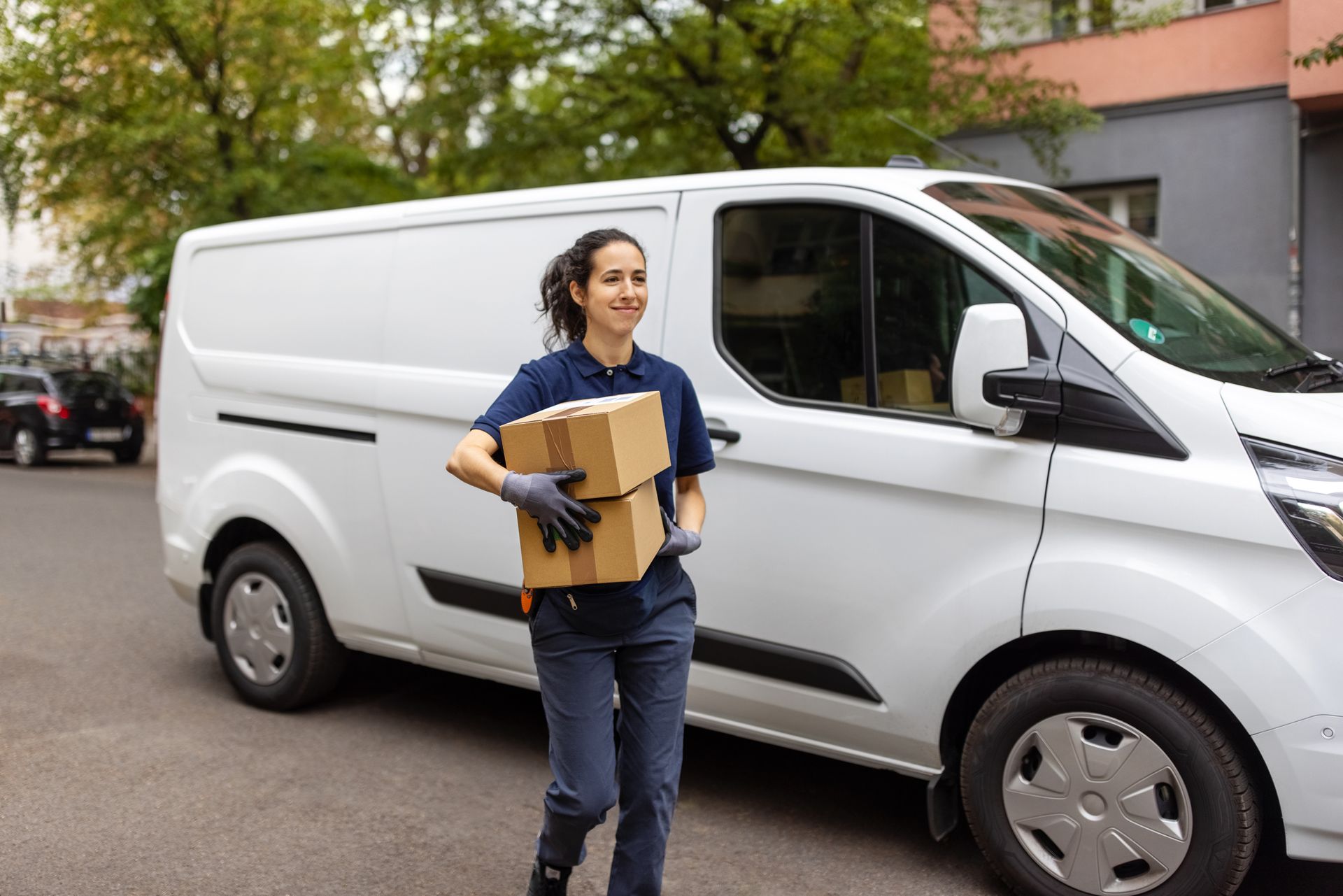 A delivery woman is carrying a box in front of a white van.