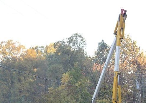 Yellow utility truck with a raised boom beside autumn trees and overhead power lines