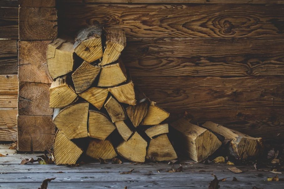 Stacked split firewood beside a rustic wooden wall, with a few logs scattered on the floor.