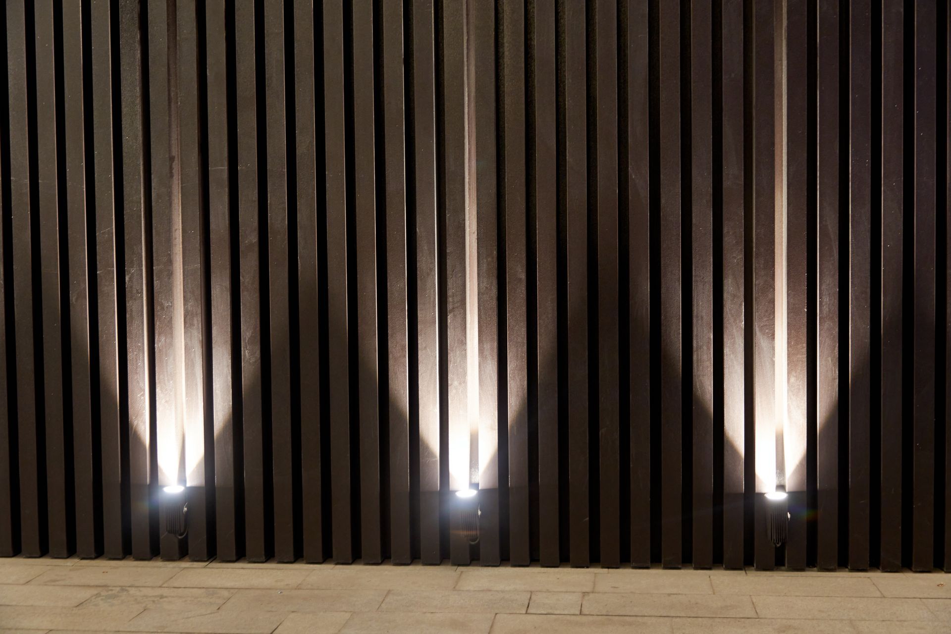 LED uplights shining against a vertical slat wall, creating bright patterns on the surface.