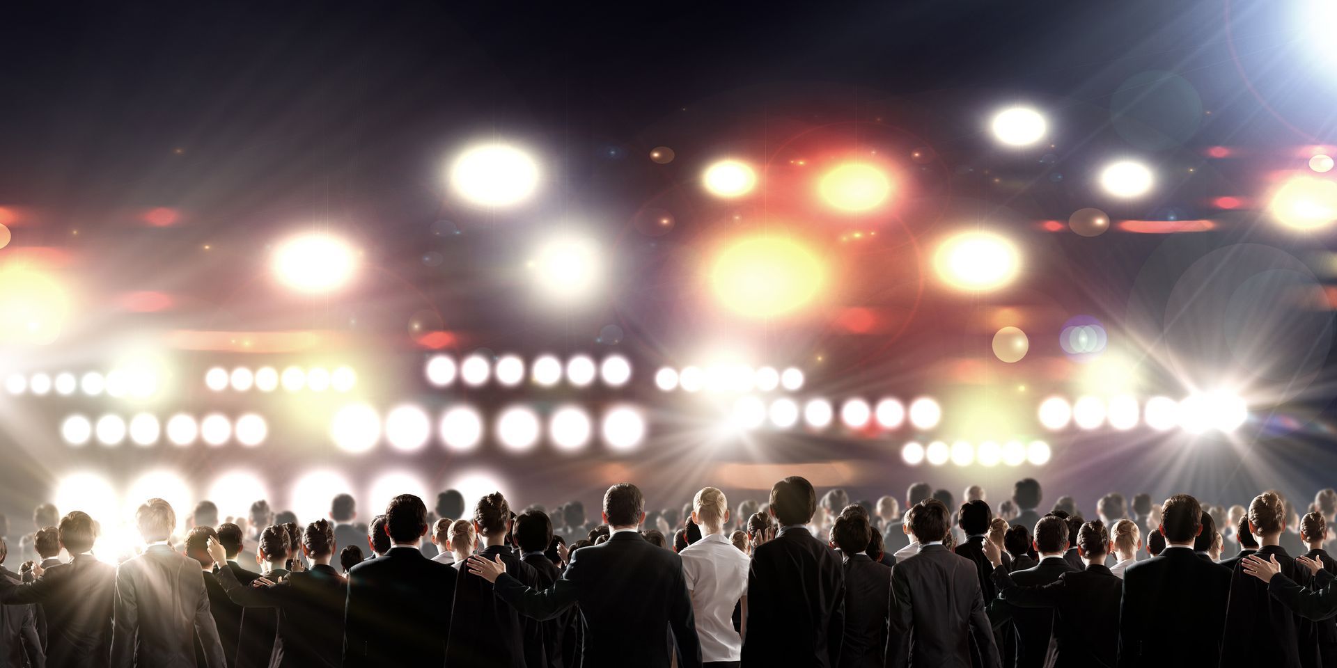 A crowd facing a stage illuminated by bright LED lighting and colorful spotlights.