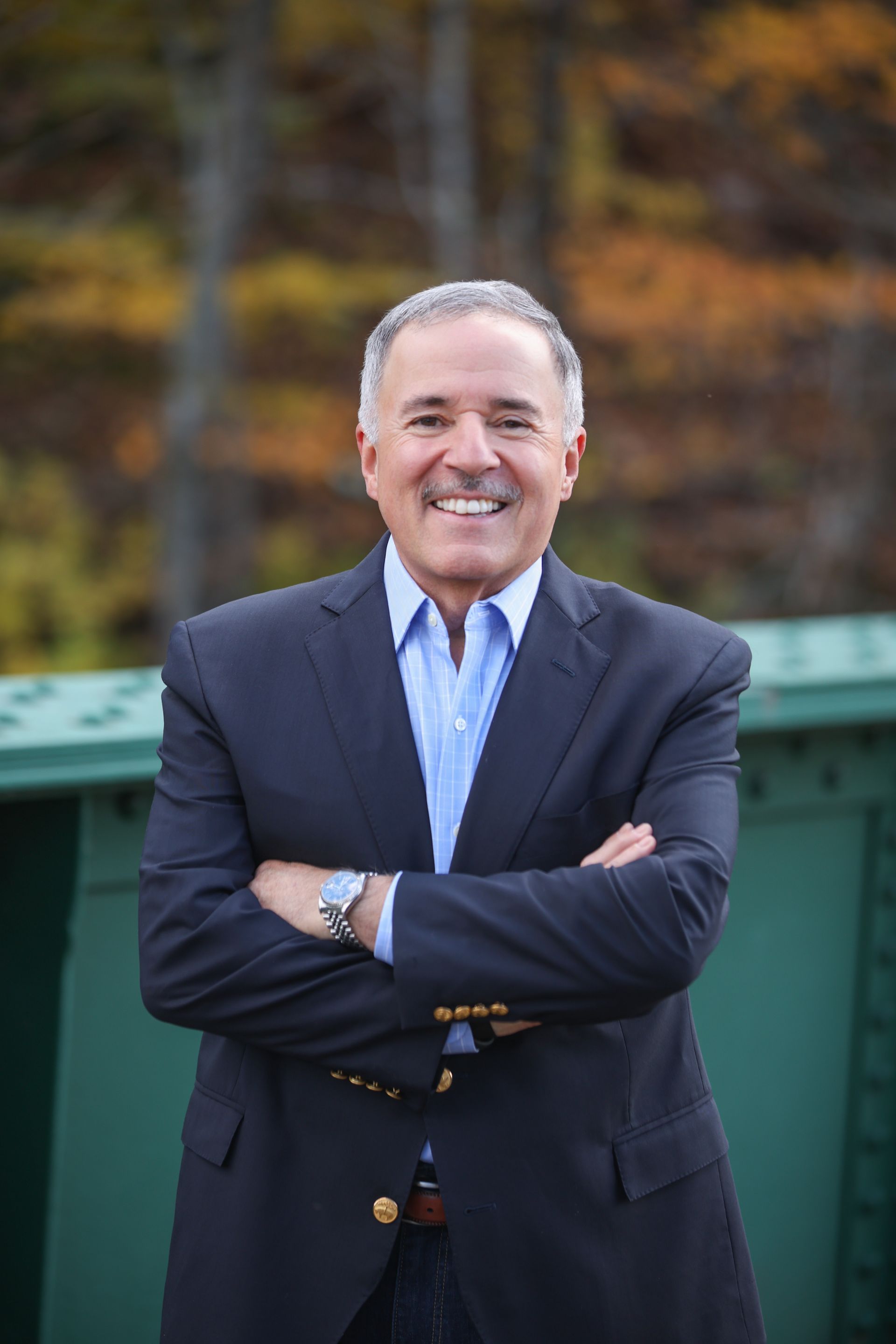 Caricature of a smiling man with a mustache in a blue suit and checked shirt, hands in pockets.