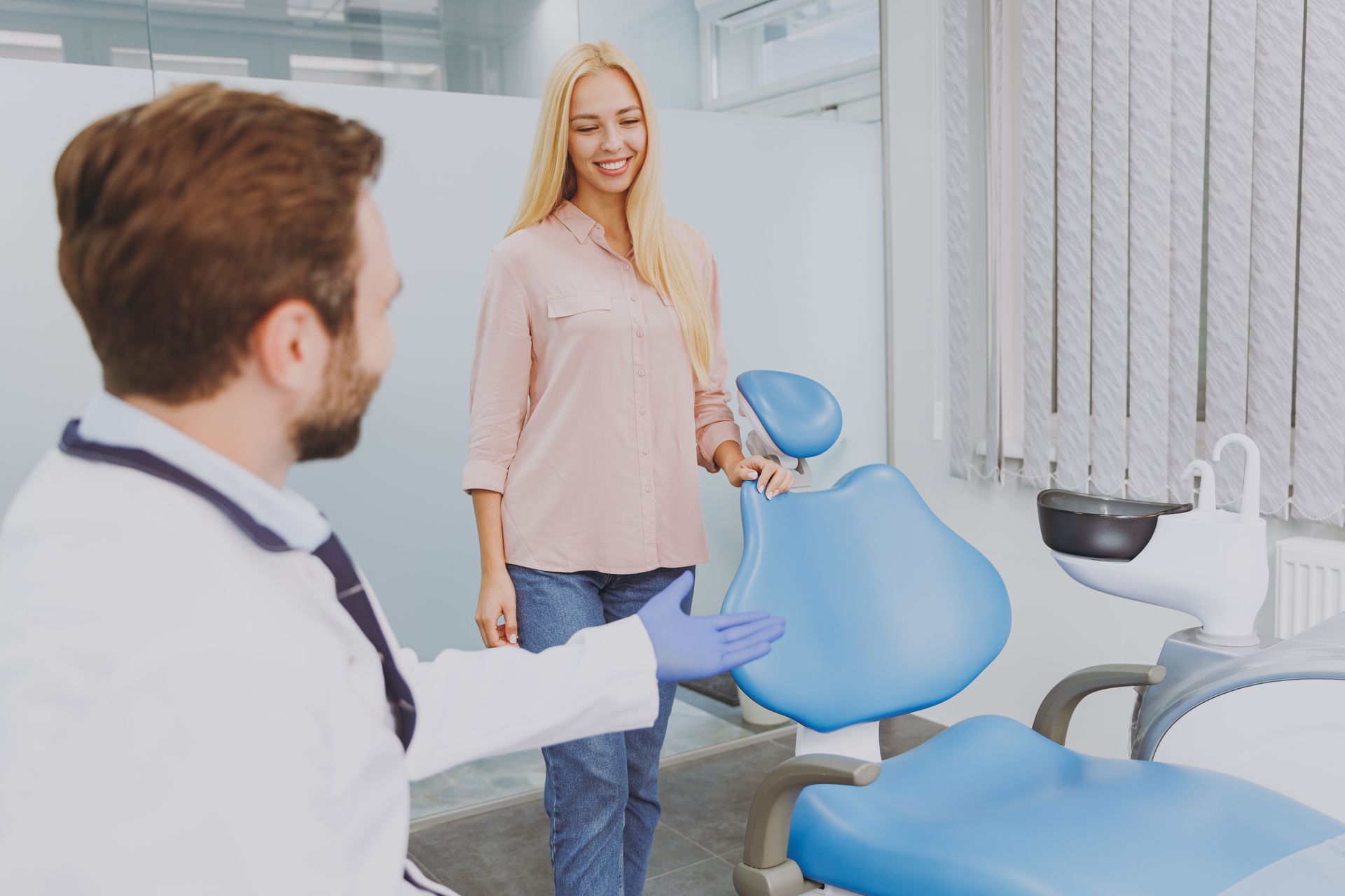 dentist gesturing for patient to take a seat in dental chair