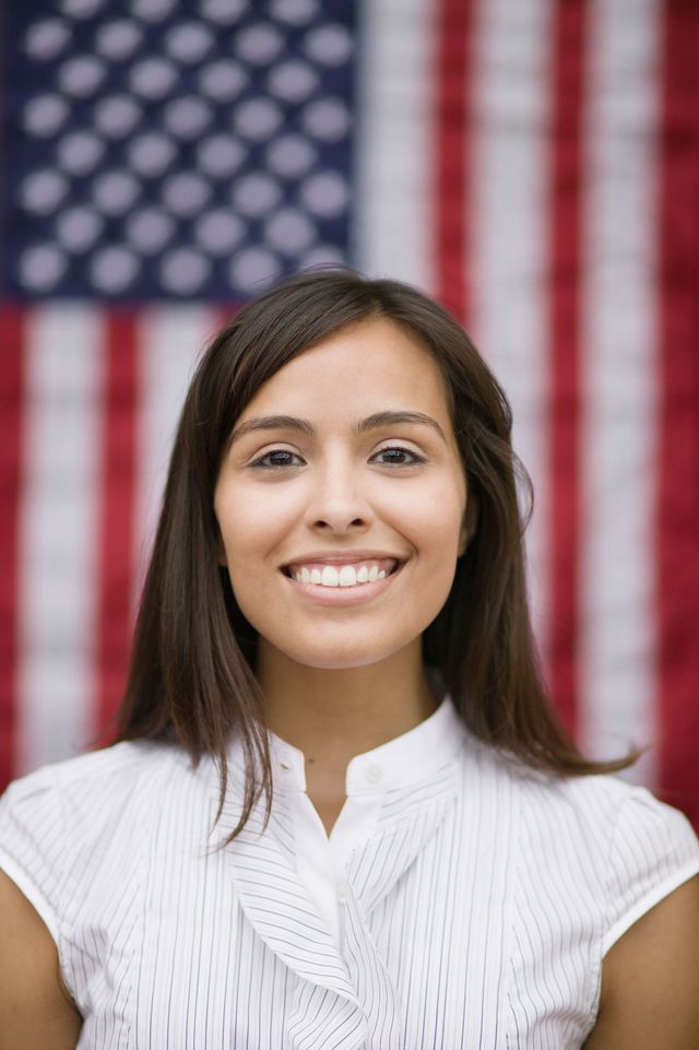 A woman is smiling in front of an american flag