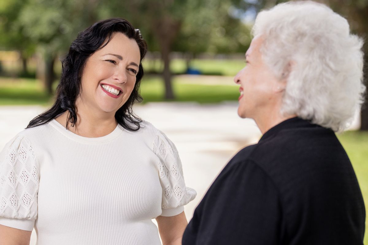 Two women are standing next to each other in a park and smiling Two women are standing next to each other in a park and smiling