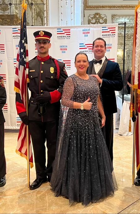 A woman in a dress is standing next to a man in a uniform holding an American flag