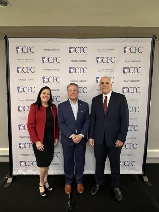 Three people are posing for a picture in front of a wall that says CFC