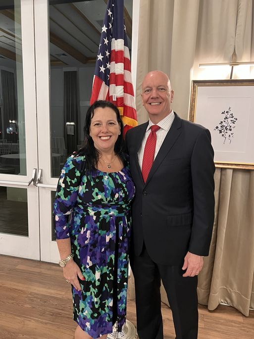 A man and a woman are posing for a picture in front of an american flag.