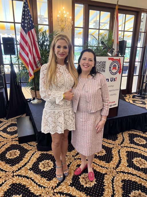 Two women are standing next to each other in a room in front of an American flag