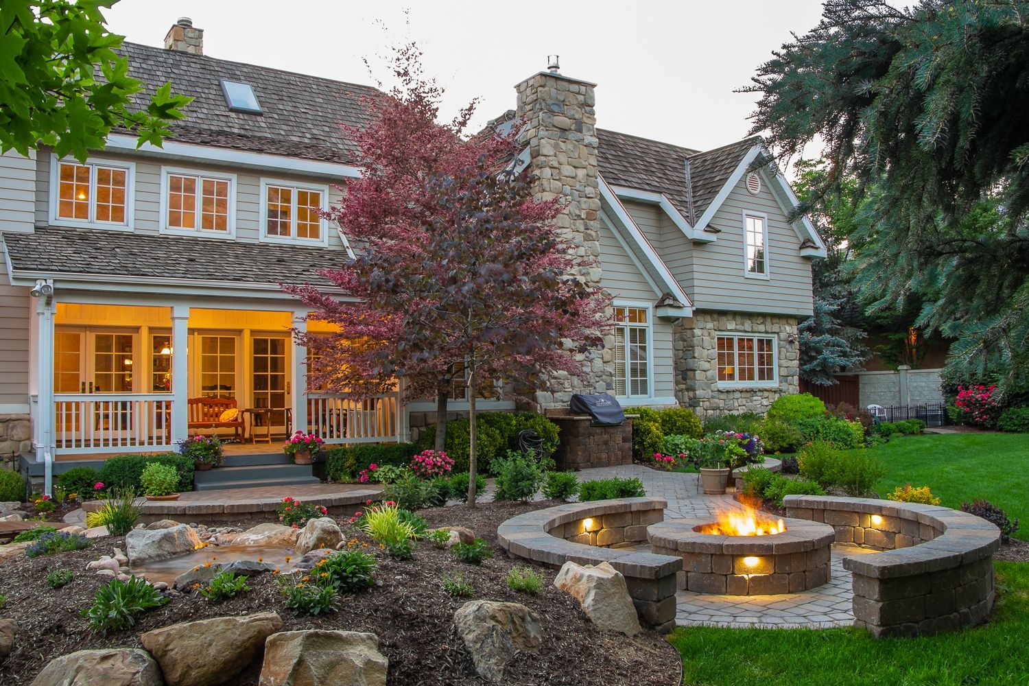 House exterior with a stone fire pit, garden, and a lawn.