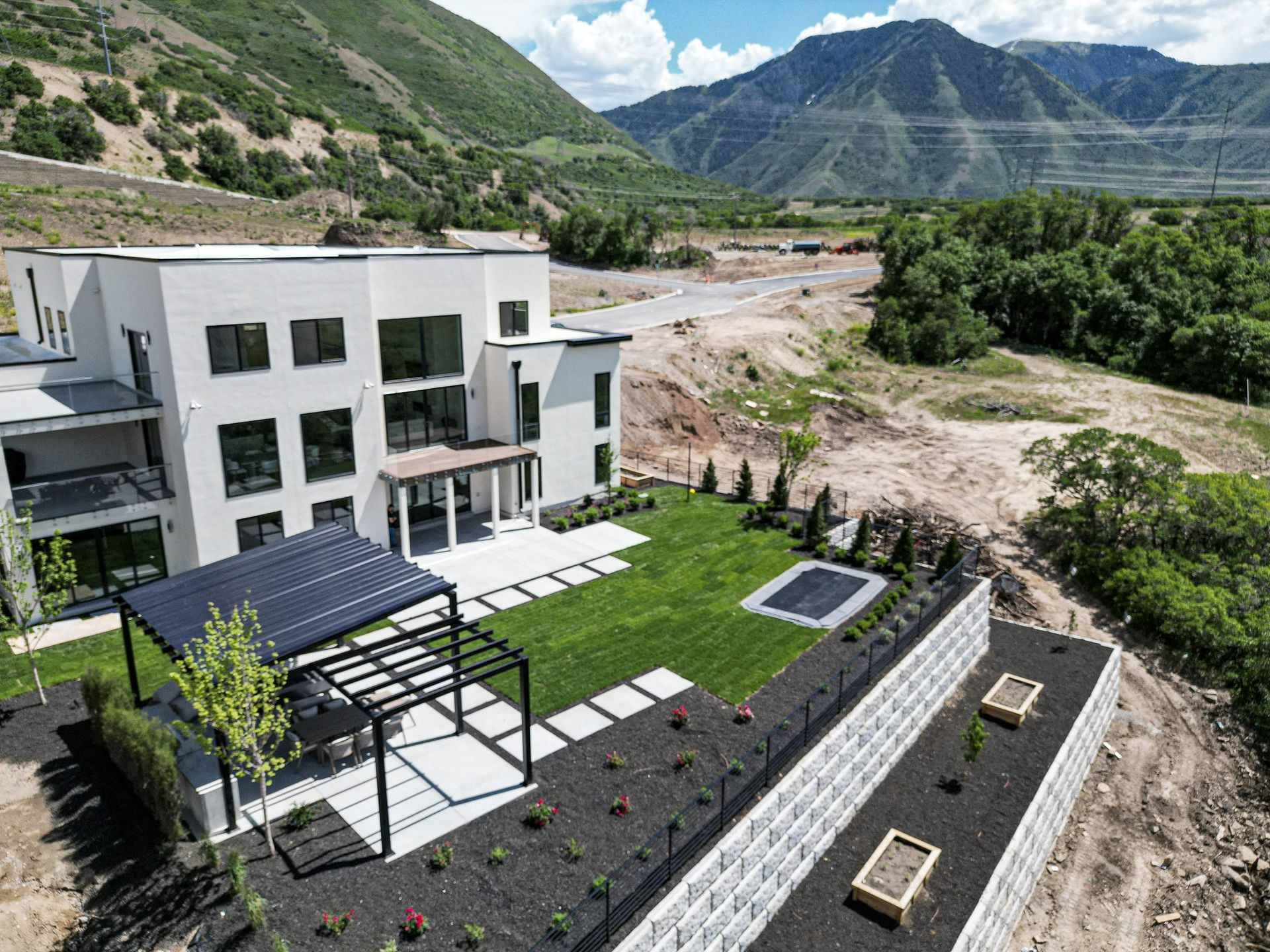 Modern home with lawn, black pergola, and retaining walls, set against a mountain backdrop.
