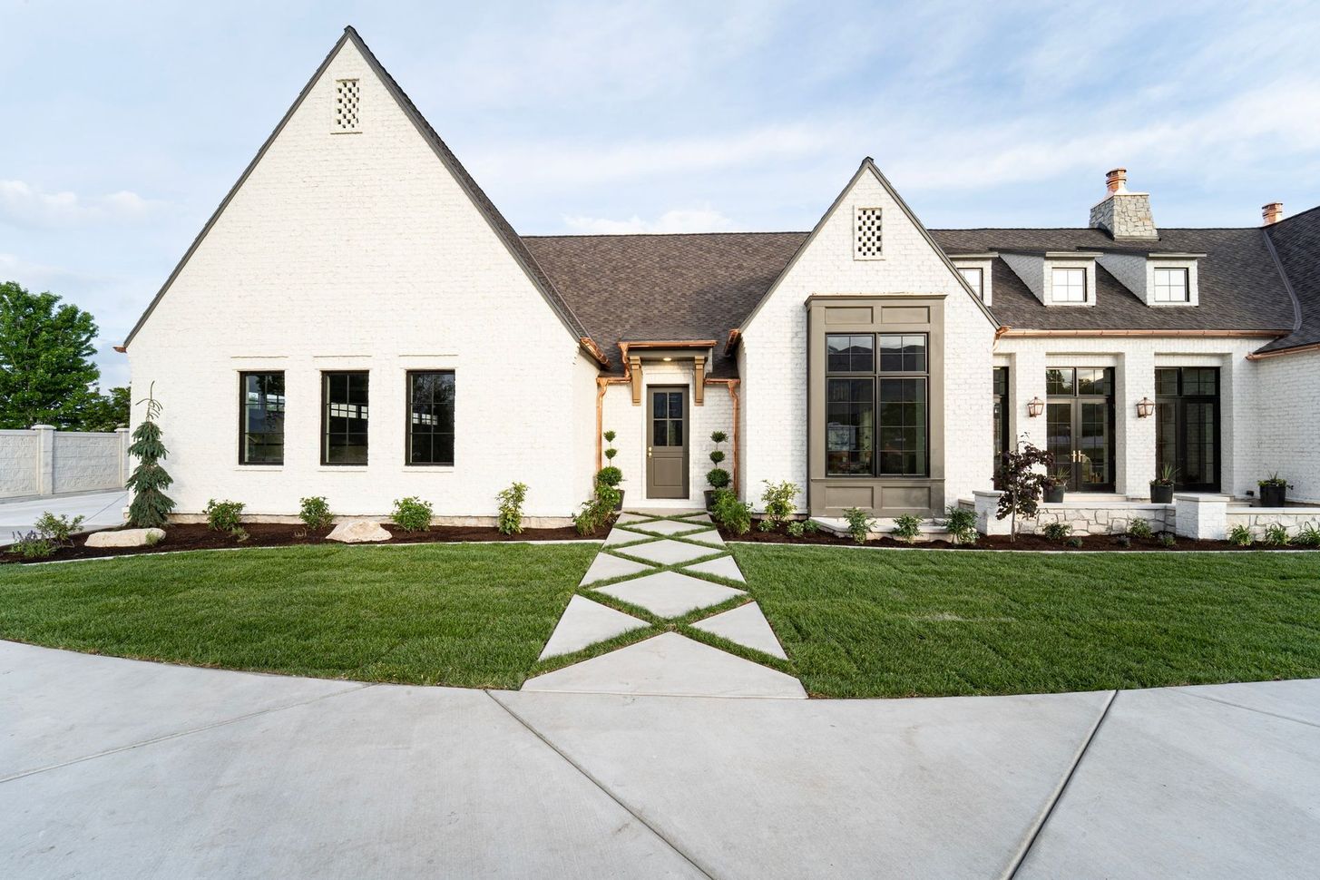 White brick house with dark roof and black window frames, green lawn, concrete path.