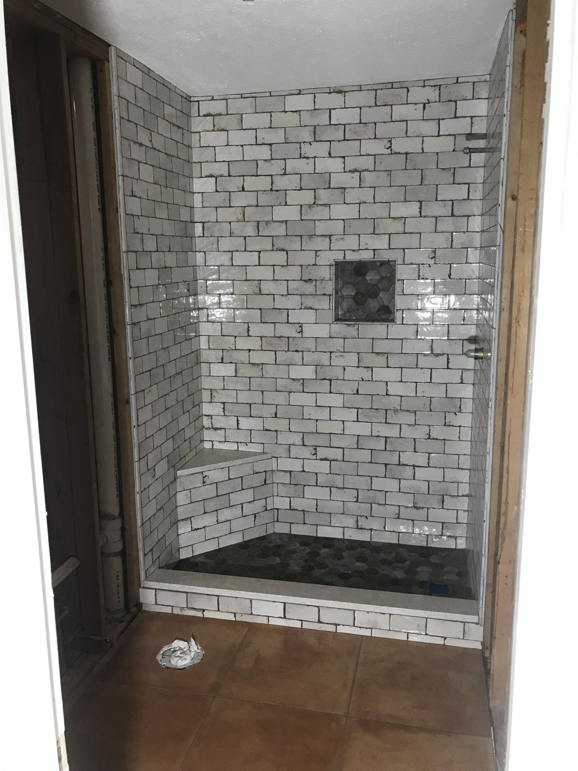A small shower with white brick-like tiles, a dark floor, and a built-in bench.