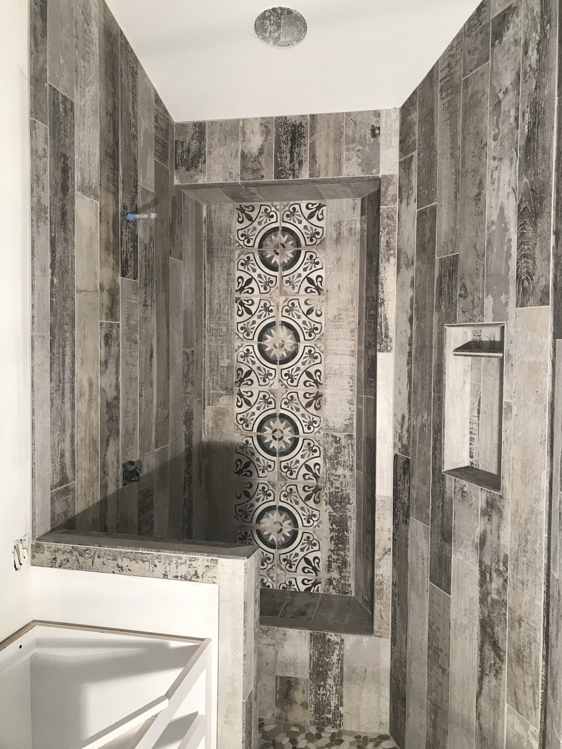 Bathroom with wood-look tile, decorative accent in recessed shower niche, and built-in shelf.