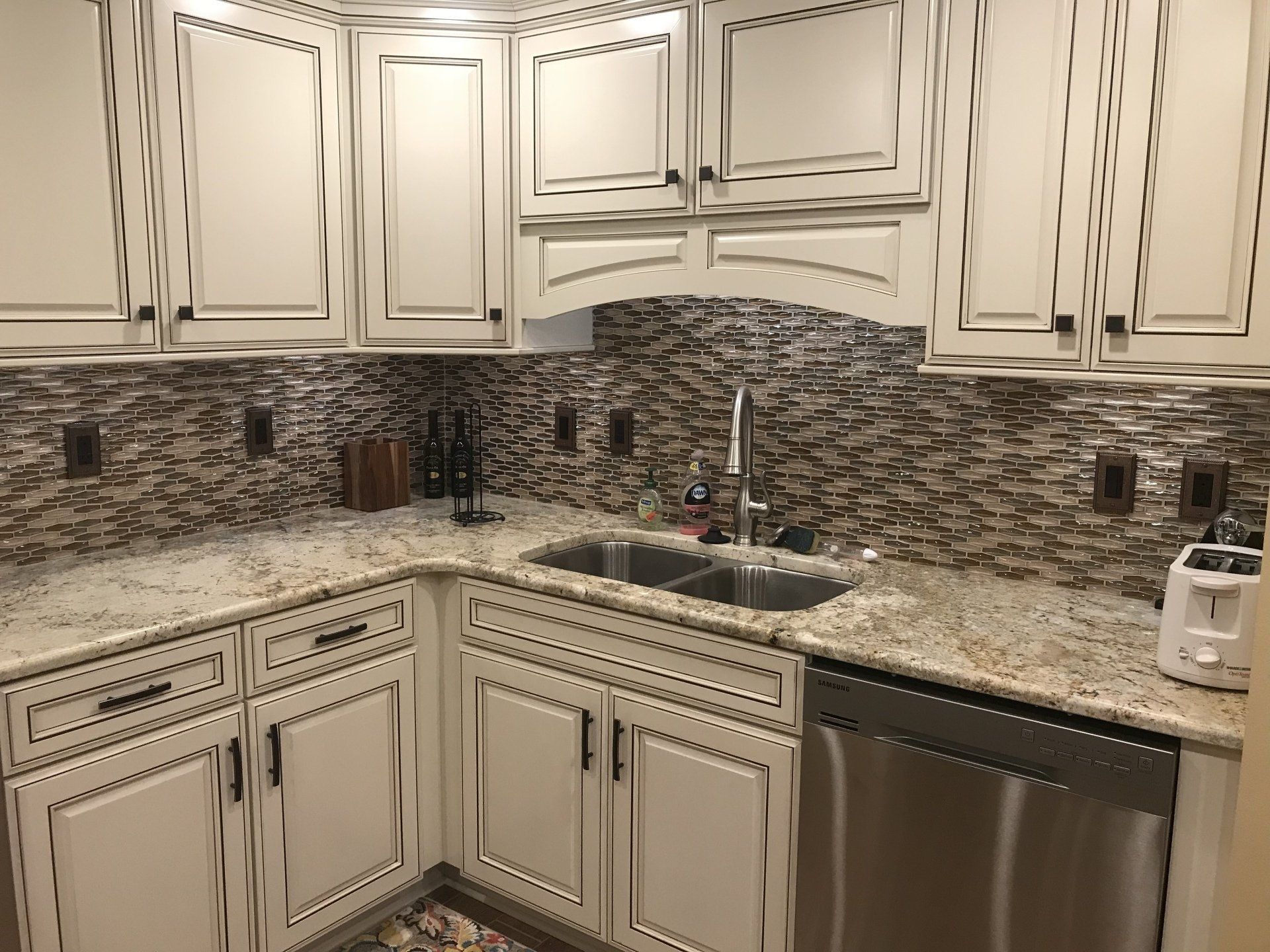 White kitchen cabinets with black accents and backsplash. Granite countertop with sink and stainless steel dishwasher.