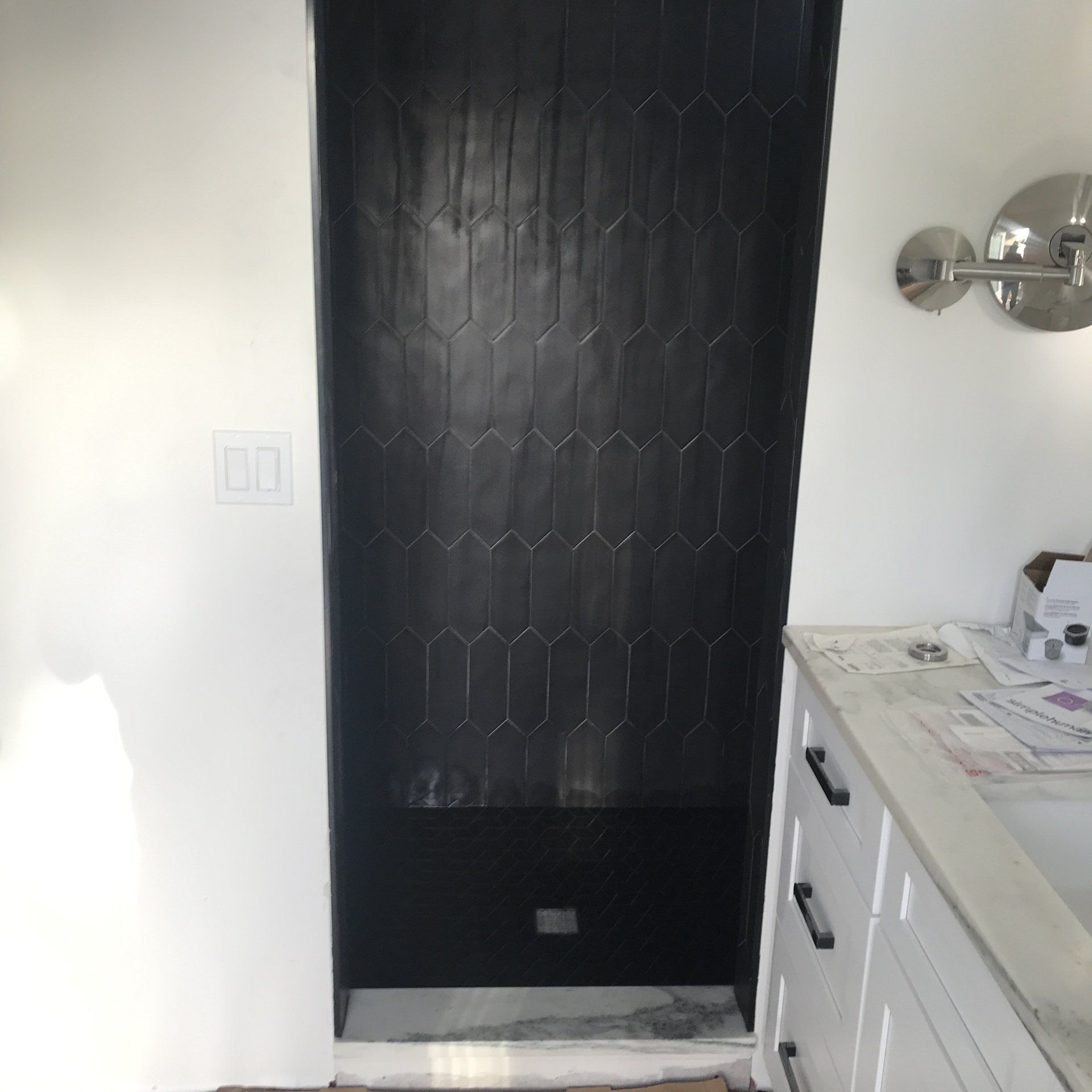 Black tile shower niche with white walls and a vanity.