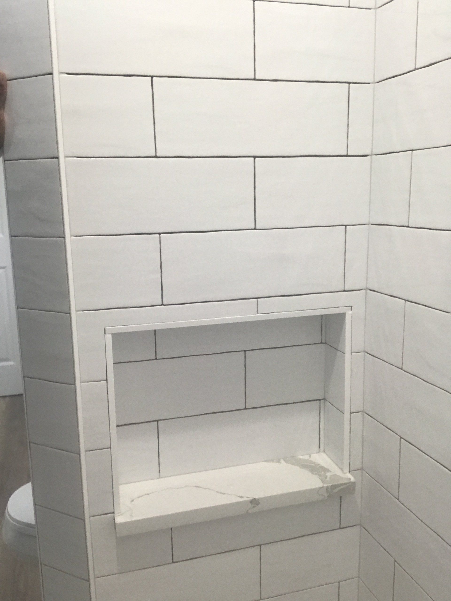 White tiled shower wall with recessed shelf, under construction.