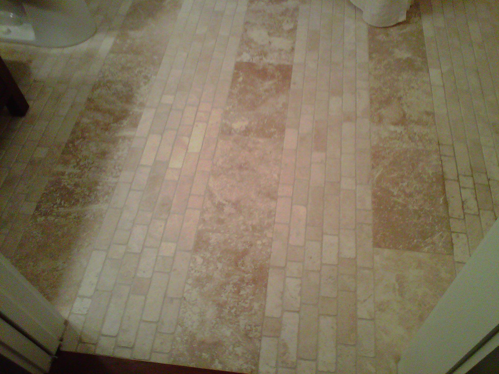 Tan and brown brick-patterned vinyl flooring in a bathroom, viewed from doorway.