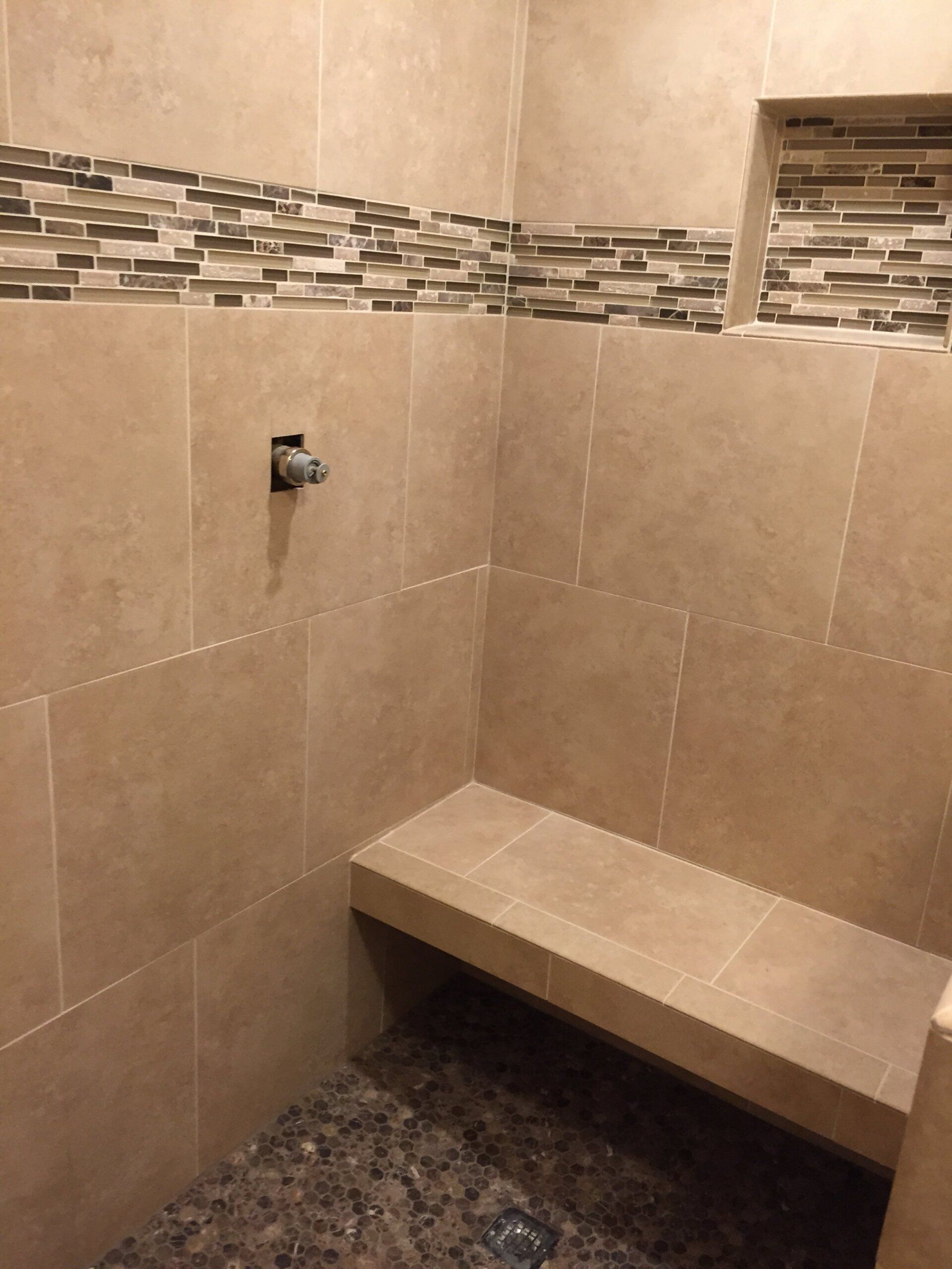 Shower with tan tiled walls, brown river rock floor, and a built-in bench.