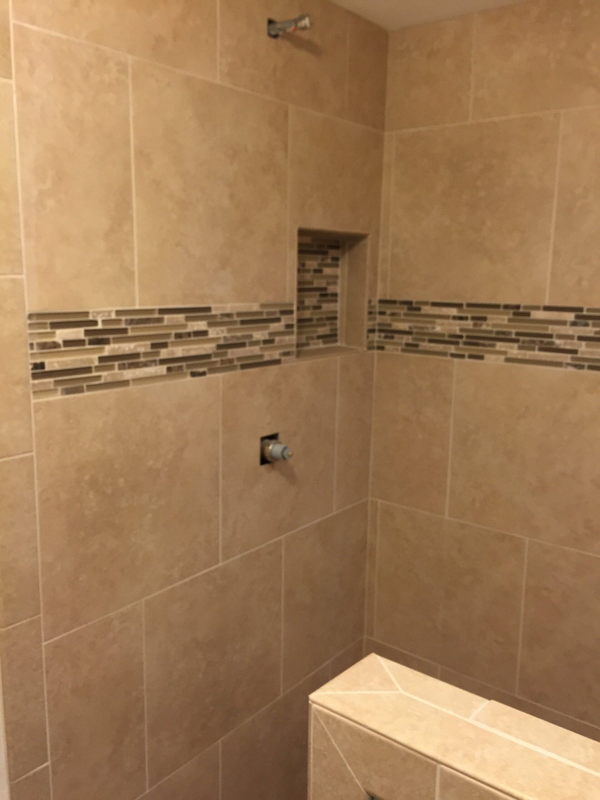 Tan tiled shower with mosaic tile stripe and built-in shelf.