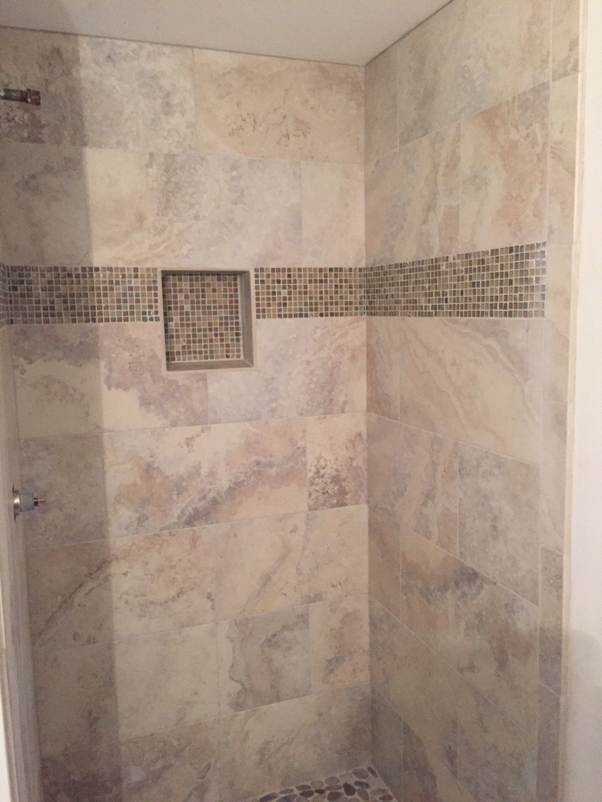 Shower stall with beige stone-look tile, mosaic accent, and built-in shelf.