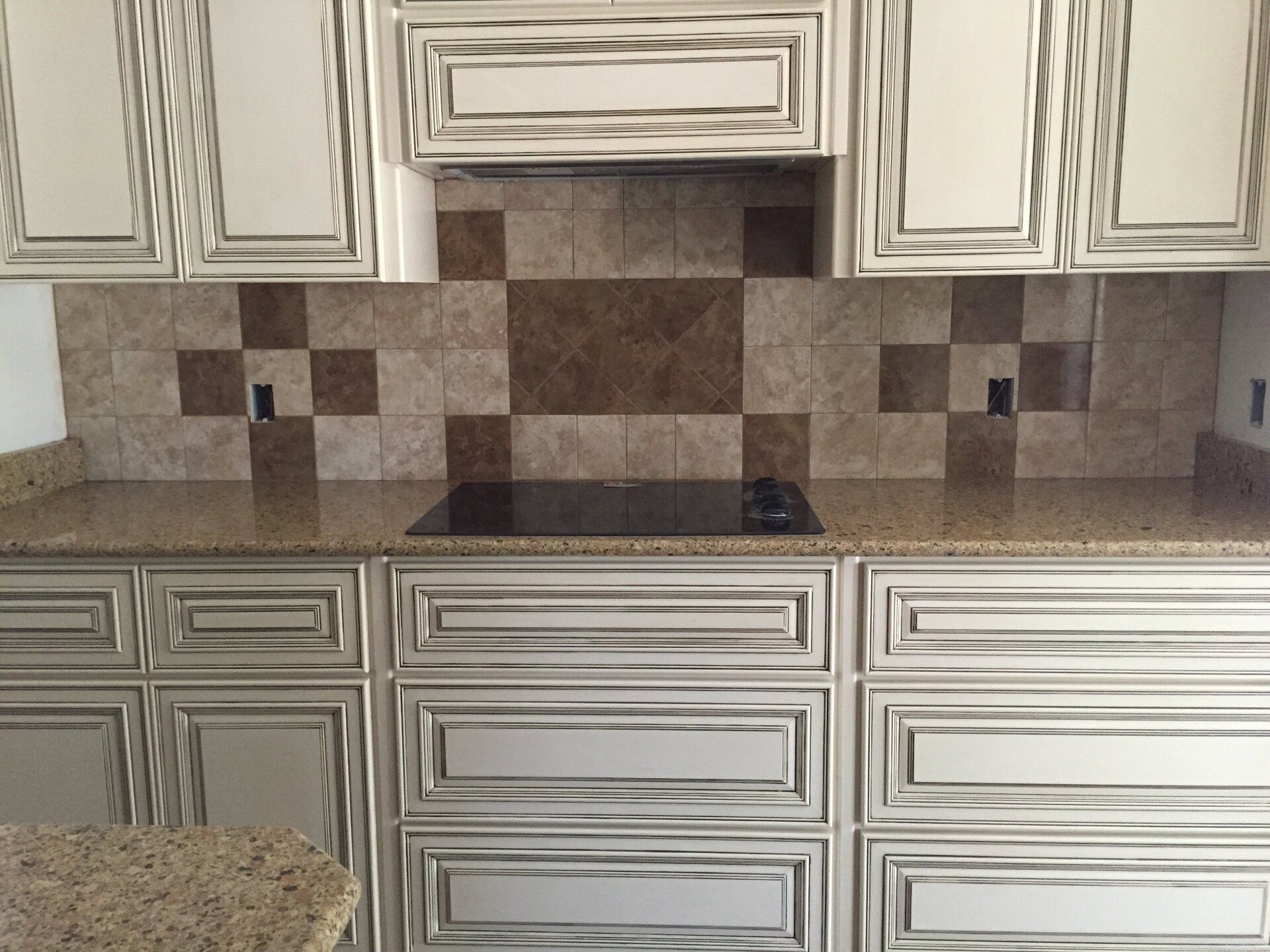 White and gray kitchen cabinets with a brown and tan tile backsplash and granite countertop.