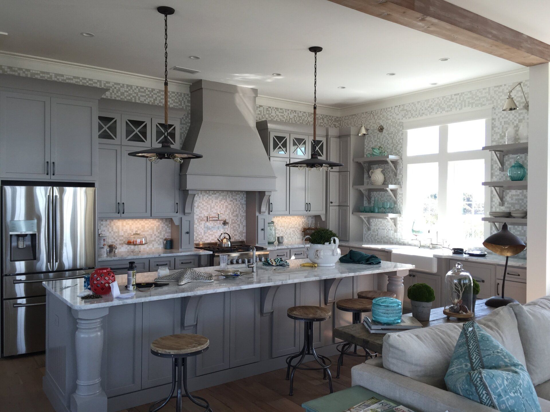 Spacious kitchen with gray cabinets, island, and stainless steel appliances. Sunlight streams through a window.