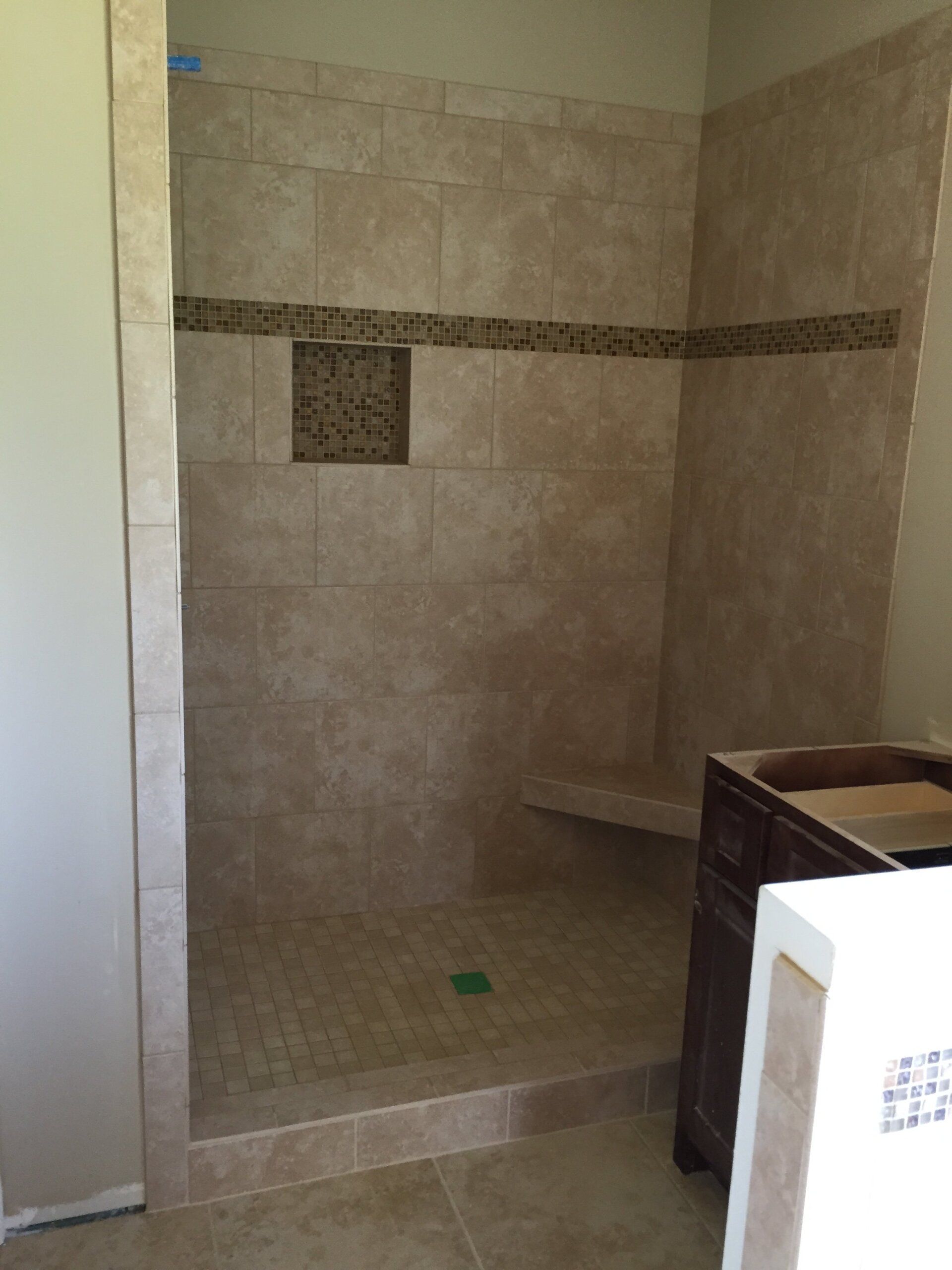 Tiled shower with a bench and niche, featuring tan tiles and a decorative mosaic band.