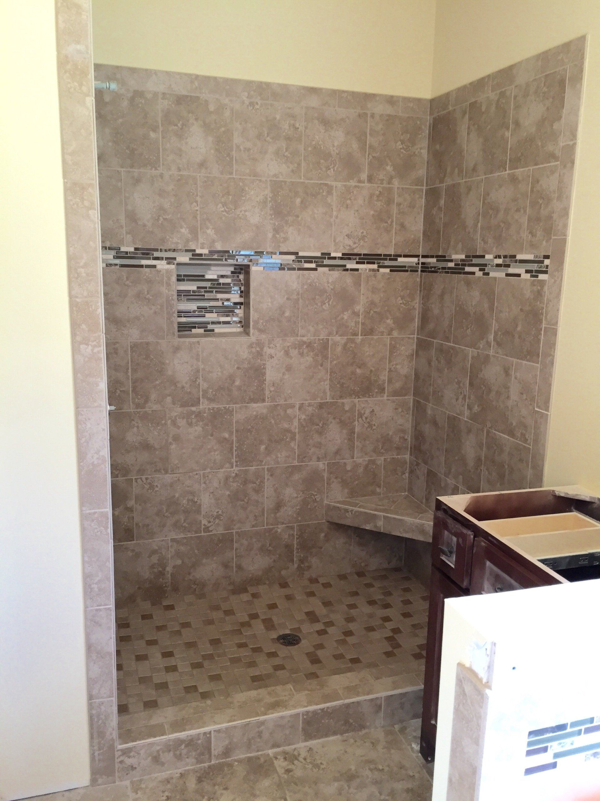 Shower stall with tan tiles, a decorative strip, a bench, and a pebble floor.