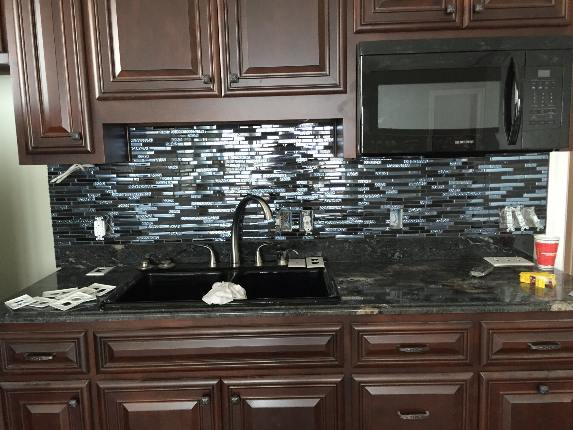 Kitchen with dark wood cabinets, black granite countertop, and mosaic tile backsplash. Black sink and microwave.
