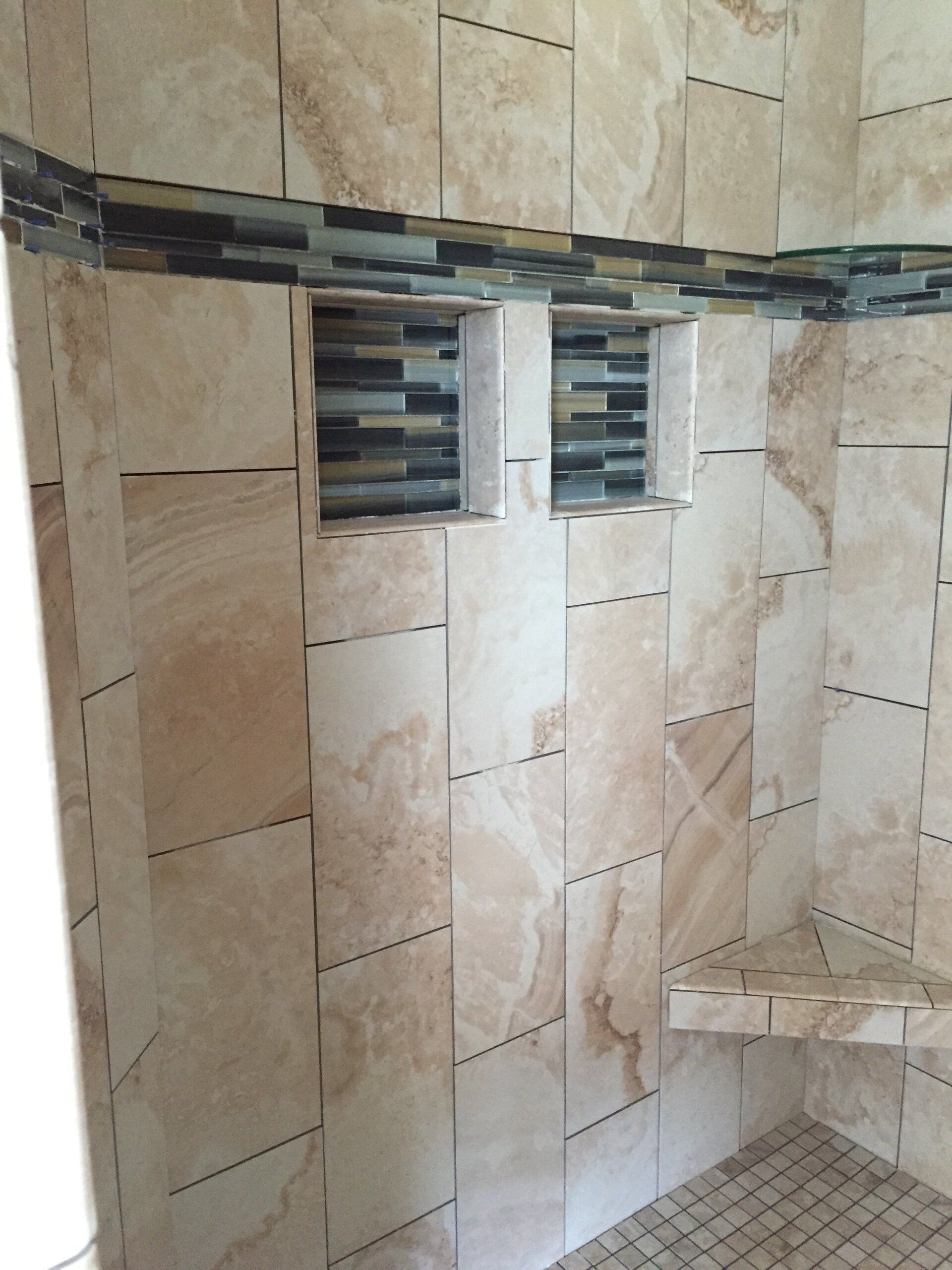 Tiled shower with beige marble-look tiles, mosaic tile accent band, recessed shelves, and a corner seat.